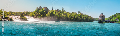 The Rhine Fall on a sunny day - Panorama with the Rhienfall, the Laufen castle and Worth Castle, while boats navigate the blue waters of the river, in Switzerland.