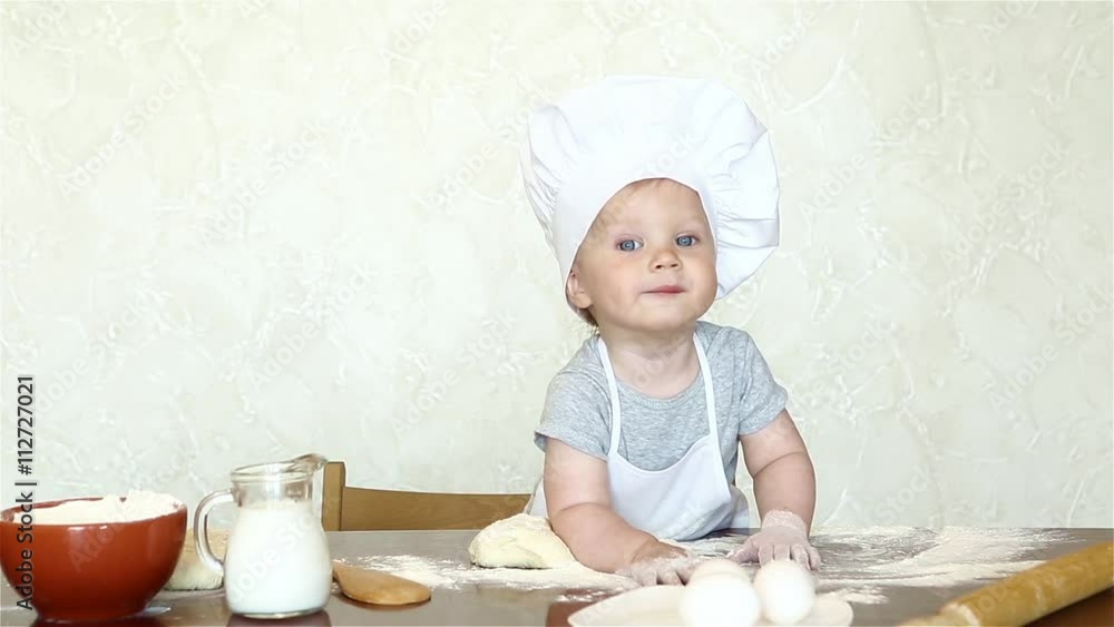 The little boy in a suit of the cook sculpts dough. Baby make dinner in chef suit The little boy in a suit of the cook sculpts dough. Baby make dinner in chef suit