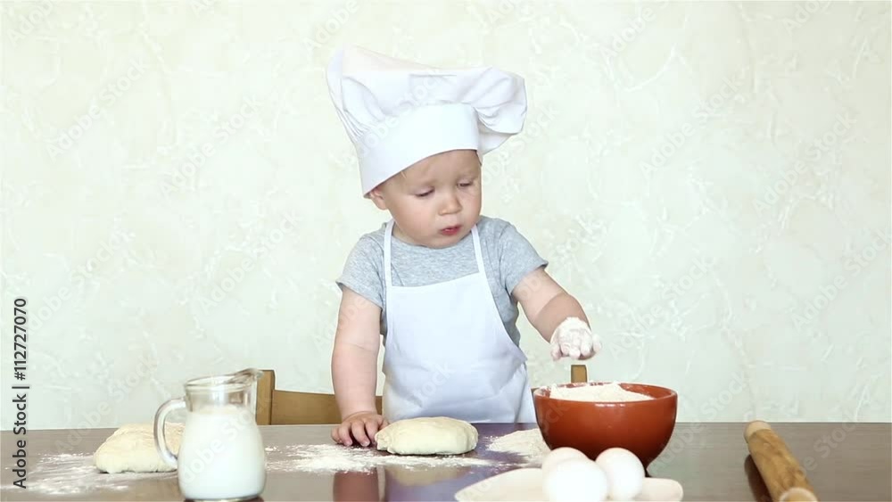 The little boy in a suit of the cook sculpts dough. Baby make dinner in chef suit The little boy in a suit of the cook sculpts dough. Baby make dinner in chef suit