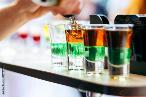 Bartender pouring alcoholic cocktail in shot glasses on bar