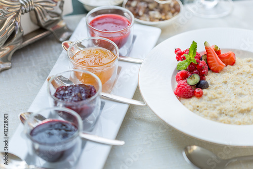 Different Berry Jam in Beautiful Glass Jars and Oatmeal with Berries, Breakfast Time in Restaurant