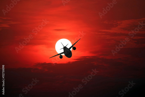 Closeup of the airplane silhouette on the beautiful sun and red sky.