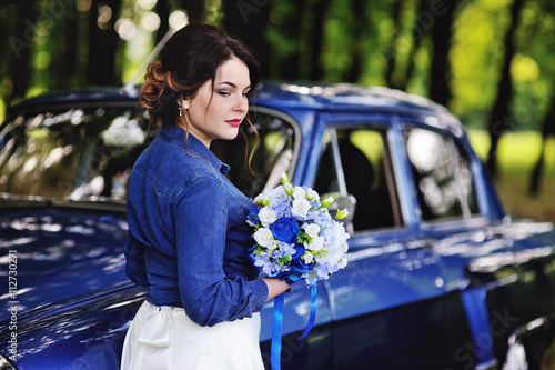 Bride in a denim jacket and with a wedding bouquet near the vint