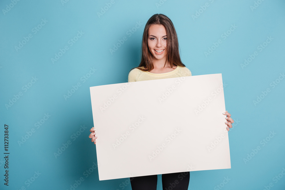 Pretty young woman holding empty blank board over blue background Pretty young woman holding empty blank board over blue background