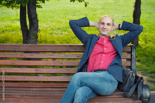 handsome bald man sitting on a bench in the park