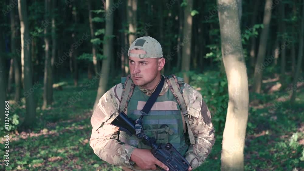 Armed young military steps in the forest and looks back. Slow motion Armed young military steps in the forest and looks back. Slow motion