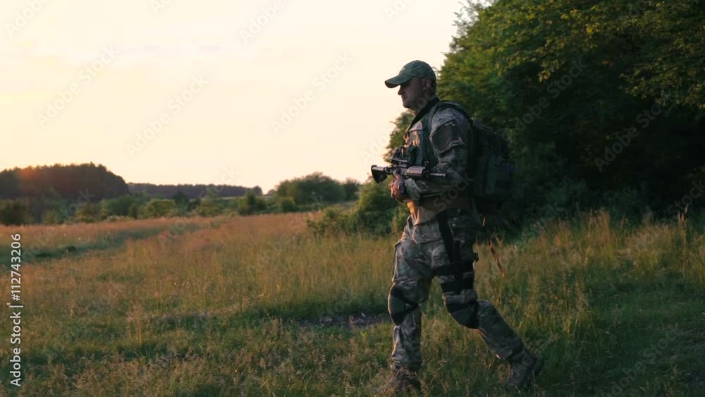 Tired soldier with automaton in hands goes on the path. Slowly Tired soldier with automaton in hands goes on the path. Slowly