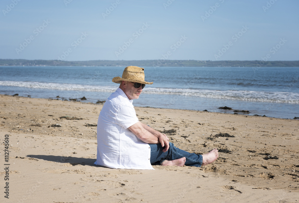 Mature man resting on a beach, looking out to sea, with a thoughtful facial expression.