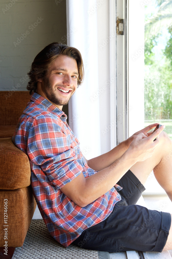 Smiling young man sitting on floor with cellphone Smiling young man sitting on floor with cellphone