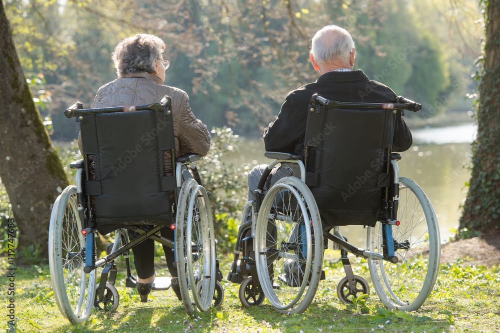 Elderly couple in wheelchairs, looking at view