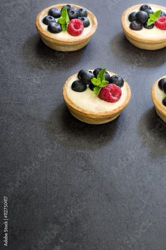 Delicious tartlets with raspberries and blueberries on slate background
