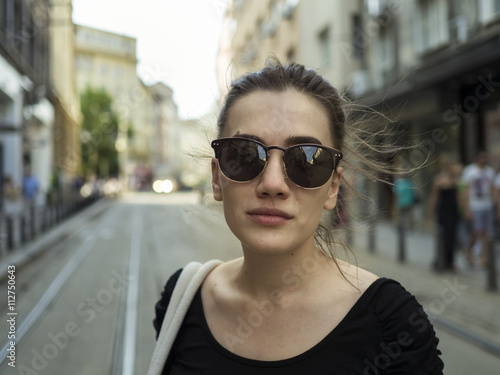Urban portrait of a beautiful young woman with sunglasses looking at the camera. Portrait on a city street of a woman wearing sun glasses.