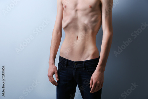 Skinny young man with anorexia on grey background