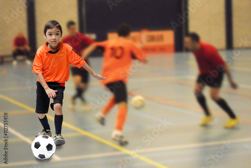 Little boy kicking football soccer ball indoor gym