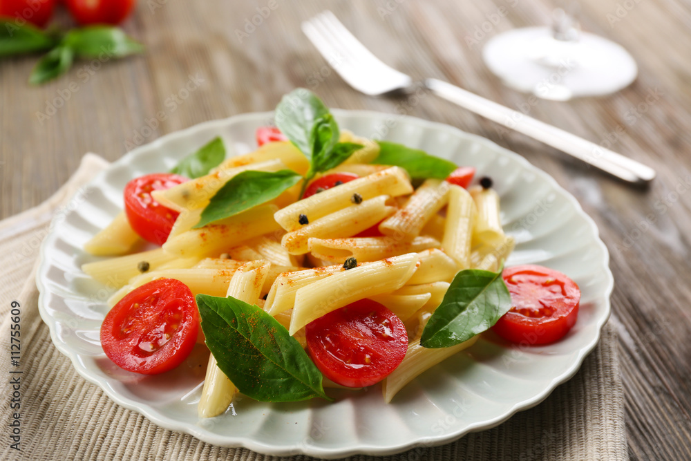 Plate of pasta with cherry tomatoes and basil leaves on table closeup Plate of pasta with cherry tomatoes and basil leaves on table closeup