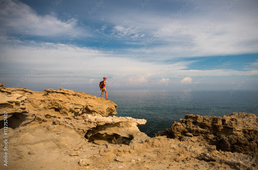 Young woman hiker standing on top of the rocks and enjoying view of a Blue Lagoon near Polis city, Akamas Peninsula National Park, Cyprus