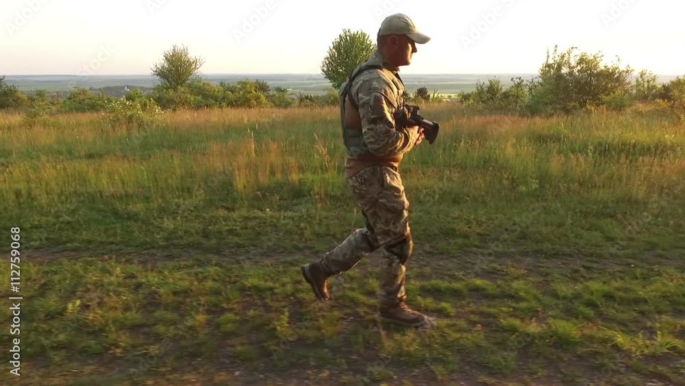 Aerial view: Armed warrior goes quickly in the field at sunset Aerial view: Armed warrior goes quickly in the field at sunset
