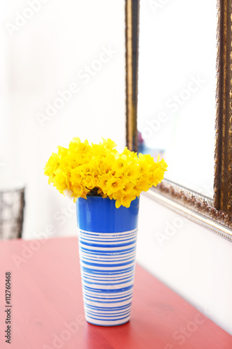 Beautiful bouquet of yellow narcissus on chest of drawers