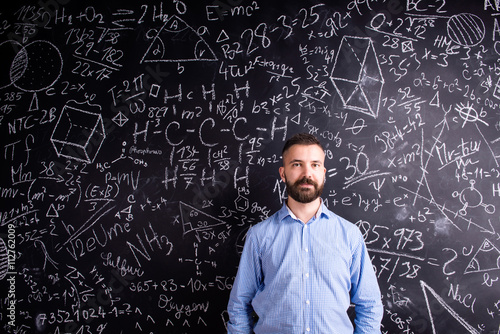 Hipster teacher against big blackboard with mathematical symbols