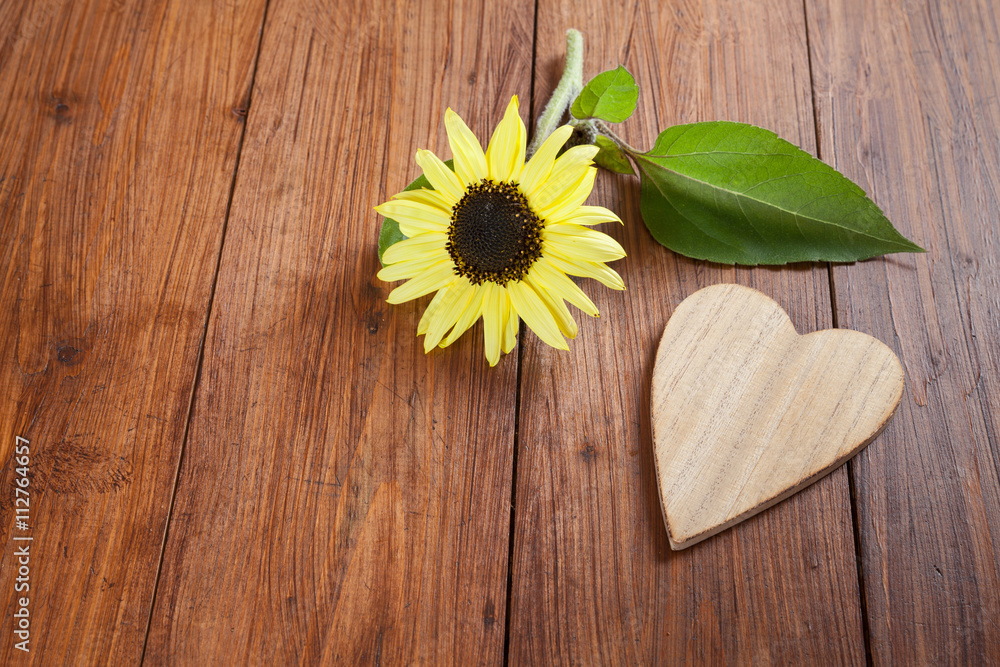 Fototapeta premium Sonnenblume und Herz aus Holz auf Holzuntergrund, Textfreiraum