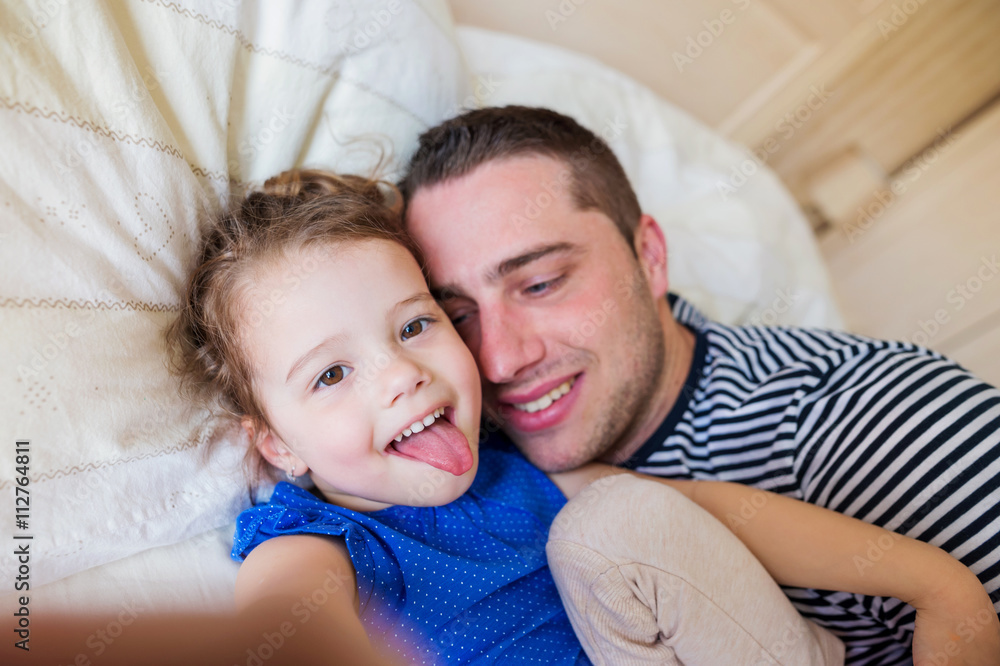 Father and daughter lying in parents bed, taking selfie Father and daughter lying in parents bed, taking selfie