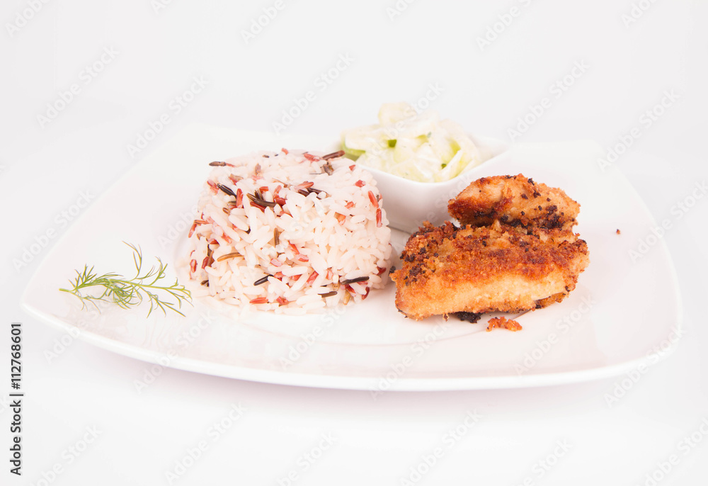 Pork chop (covered in breadcrumbs), three color rice and cucumber salad decorated with dill on a plate on white background