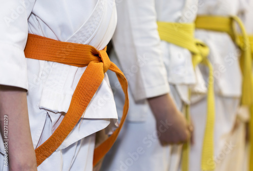 Children with colored belts in kimono sitanding in a line on martial arts class. Selective focus