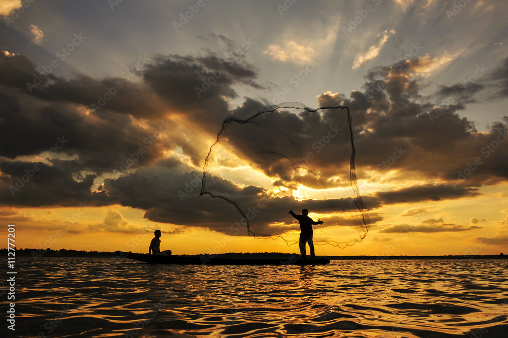 A fisherman casting a net into the water during on sunset