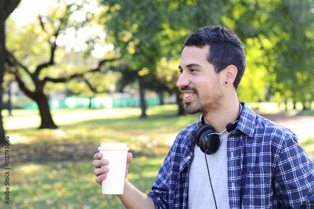 Young man with headphones and drinking coffee in a park. Young man with headphones and drinking coffee in a park.