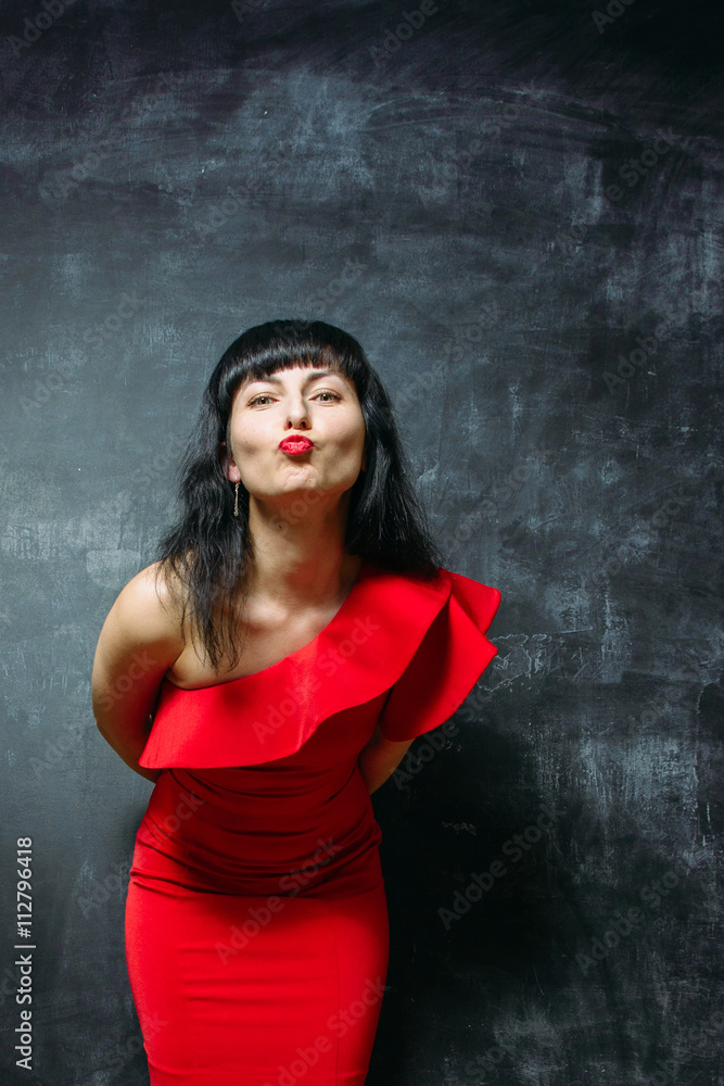 Beautiful young model woman in red dress posing over black slate Beautiful young model woman in red dress posing over black slate