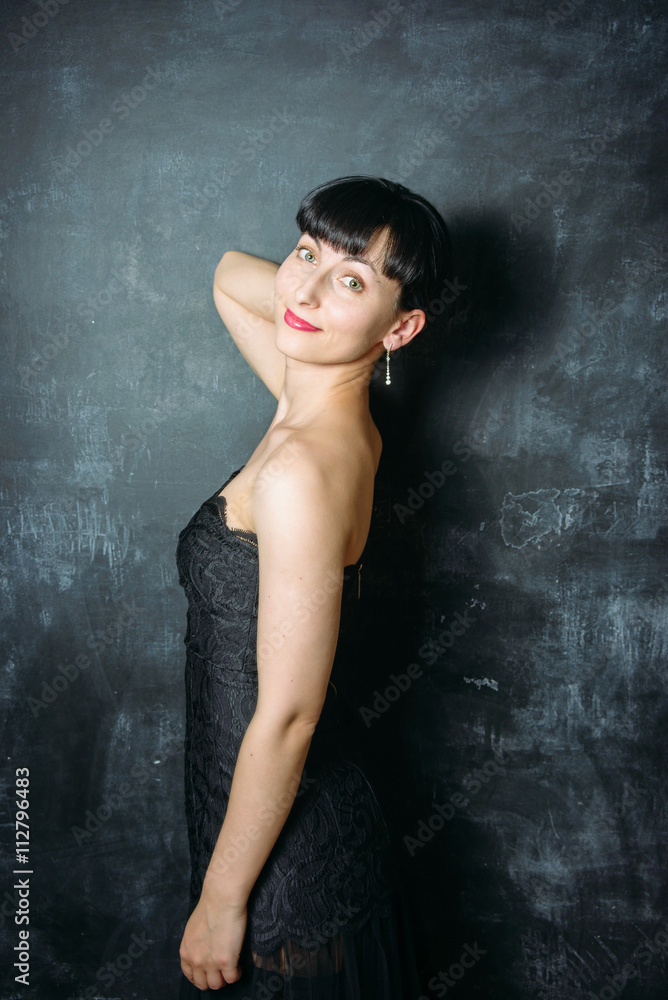 Beautiful young model woman in black dress posing over black sla
