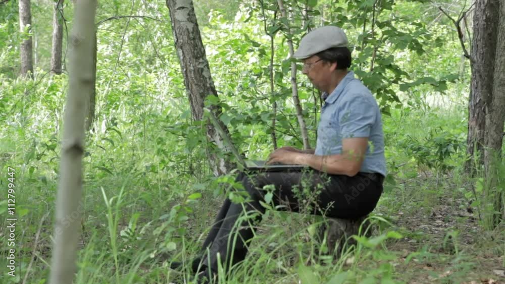 Man working remotely with laptop in nature, sitting in the forest Man working remotely with laptop in nature, sitting in the forest