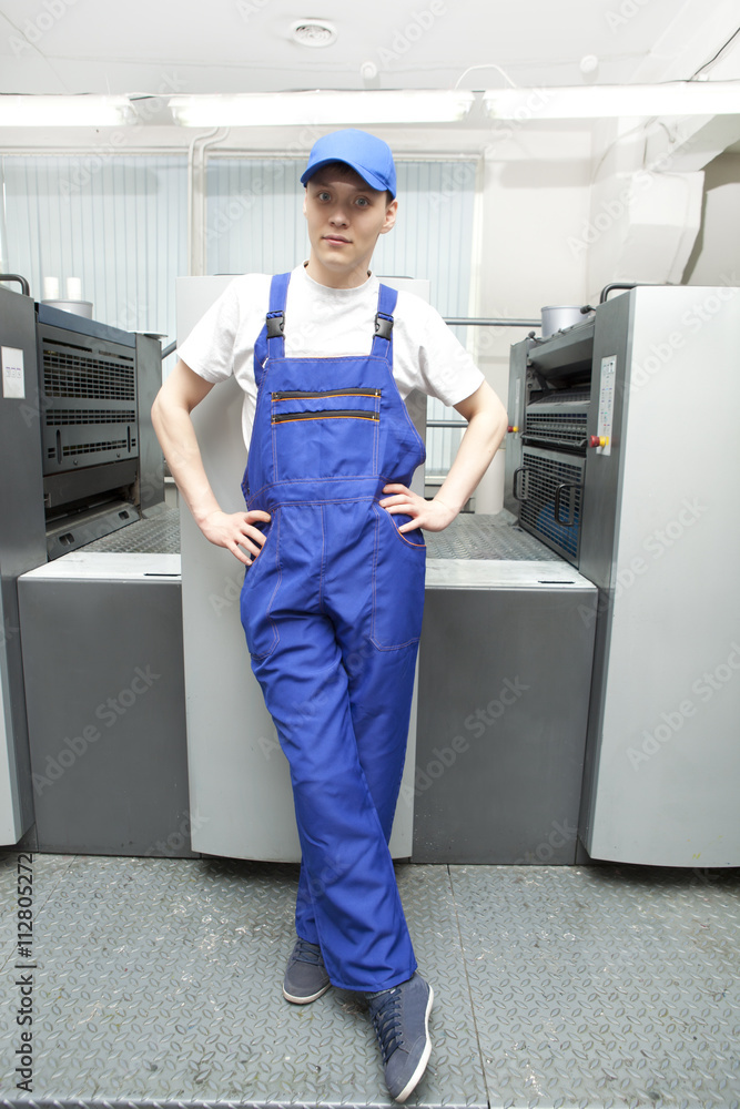 Young man in cap working on offset printing machine Young man in cap working on offset printing machine
