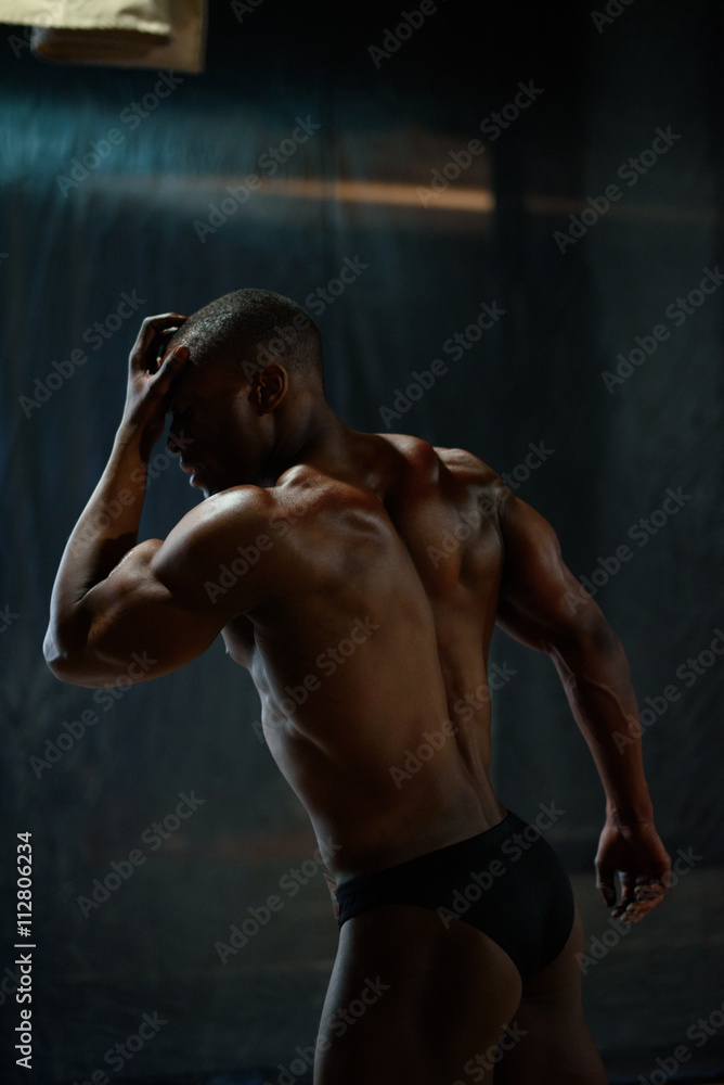 Obraz premium Portrait of handsome african american male body builder with naked torso posing on a black studio background.