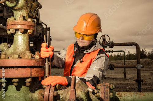 Woman engineer in the oil field repairing wellhead with the wrench wearing orange helmet and work clothes. Oil and gas concept. Toned.