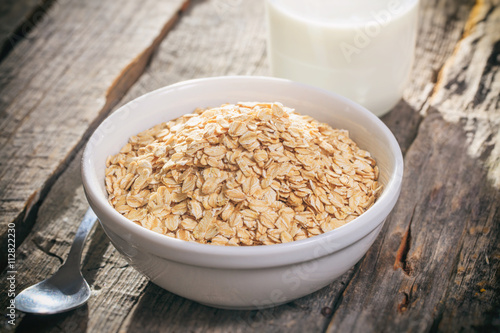 Bowl of oat flakes and glass of milk, on wooden surface. © viperagp