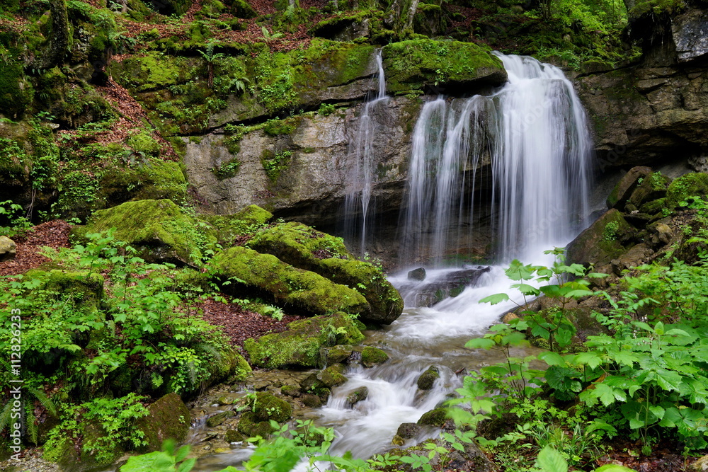 Kleiner Wasserfall im Wald mit Moos auf Steinen