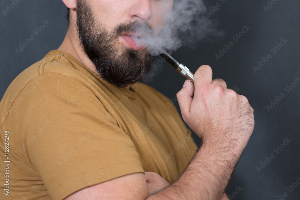 Fototapeta premium Black haired handsome man vaping e-cirarette mod - blowing cloud