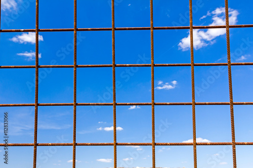 View on blue sky trough steel reinforcement square rusty bars.