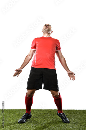 young happy football player in red jersey screaming excited on grass pitch celebrating scoring goal