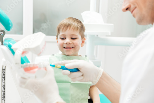 Dentist teaching little boy how to cleaning teeth