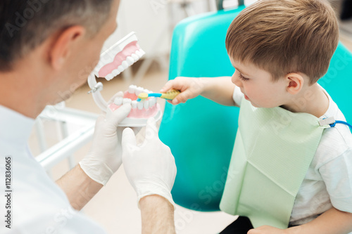 Dentist teaching little boy bruching teeth in dental clinic