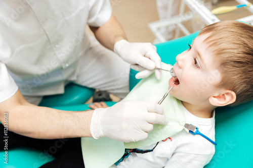 Dentist examining little boy teeth with mirror and hook