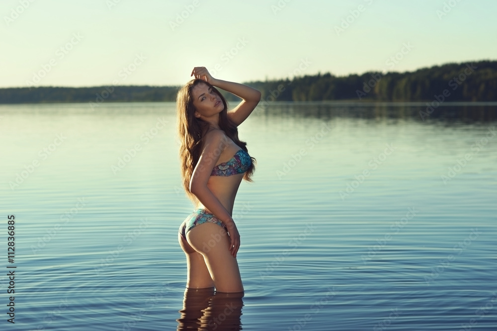 Stunning beautiful girl posing in blue bikini in the lake. Young sexy woman. Full length portrait at sunset with soft lightning Stunning beautiful girl posing in blue bikini in the lake. Young sexy woman. Full length portrait at sunset with soft lightning