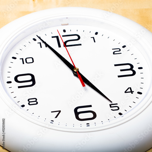 White wall clock with black arrows. Selective focus. Shallow dep