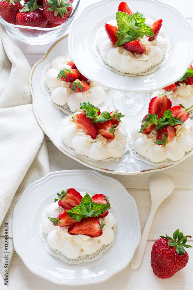 Homemade small strawberry pavlova meringue cakes with mascarpone cream and fresh mint leaves on white plate Homemade small strawberry pavlova meringue cakes with mascarpone cream and fresh mint leaves on white plate