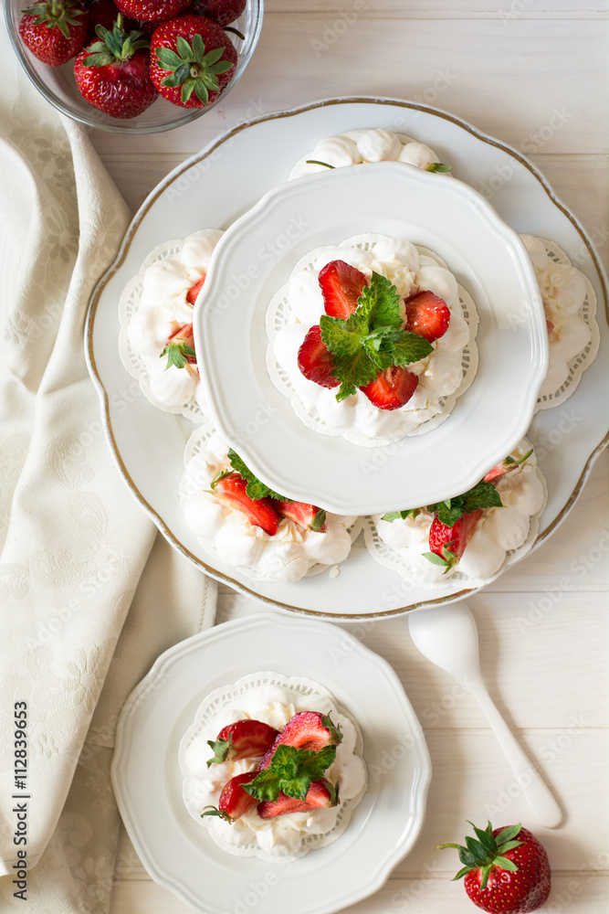 Homemade small strawberry pavlova meringue cakes with mascarpone cream and fresh mint leaves on white plate Homemade small strawberry pavlova meringue cakes with mascarpone cream and fresh mint leaves on white plate