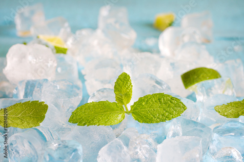 Ice cubes and fresh mint leaves abstract background on blue boards 