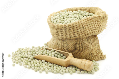 green peas in a burlap bag with a wooden scoop on a white background