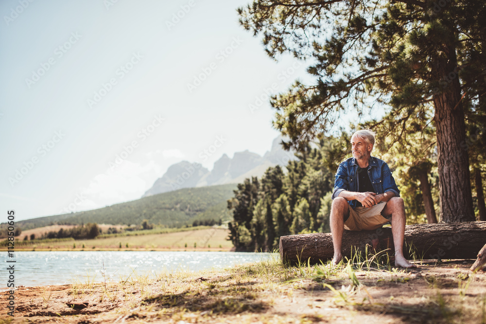 Mature man sitting on wooden log by the lake Mature man sitting on wooden log by the lake